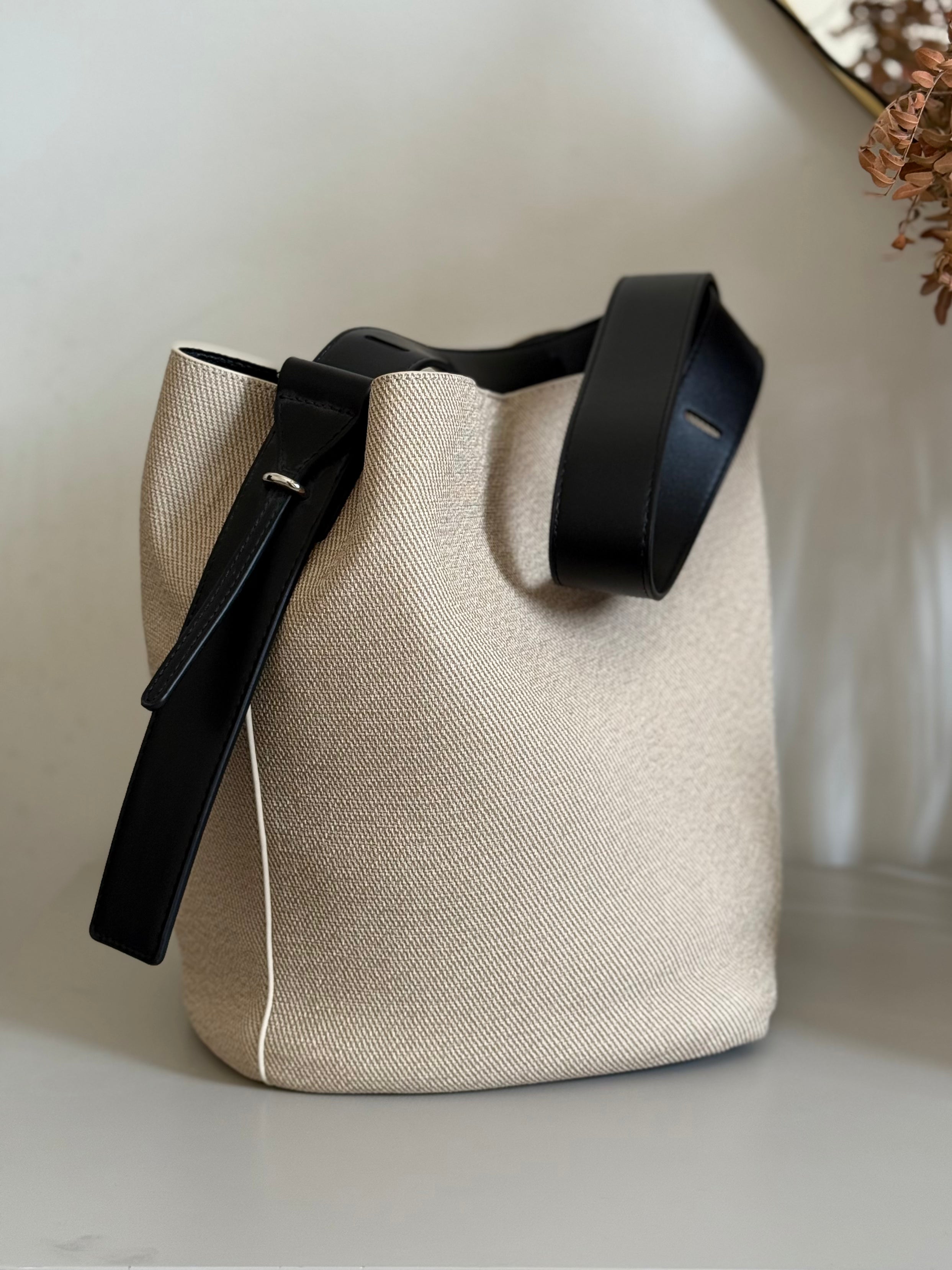 Beige fabric bucket bag with black leather trim.