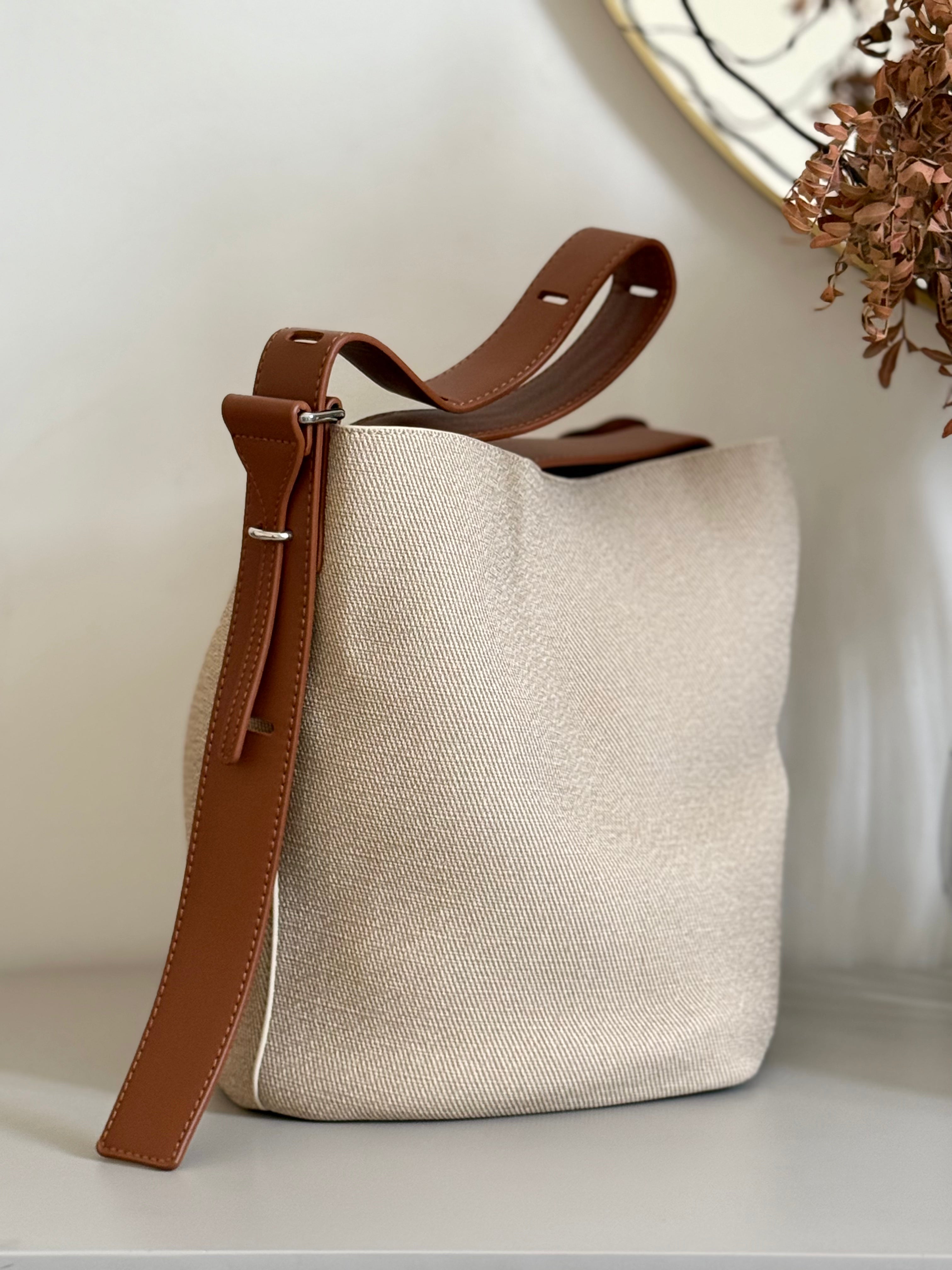 Beige fabric bucket bag with black leather trim.