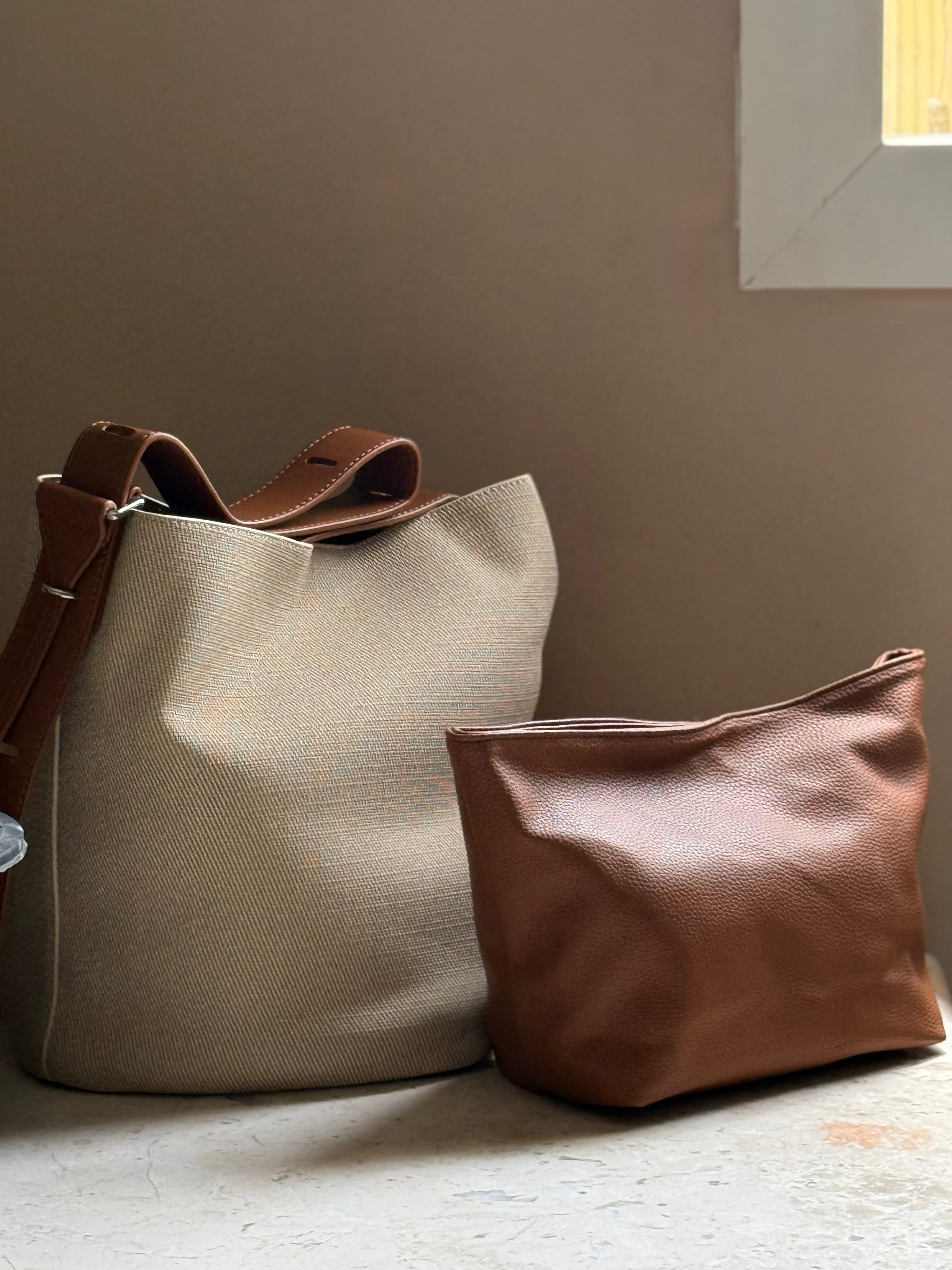 Beige fabric bucket bag with black leather trim.